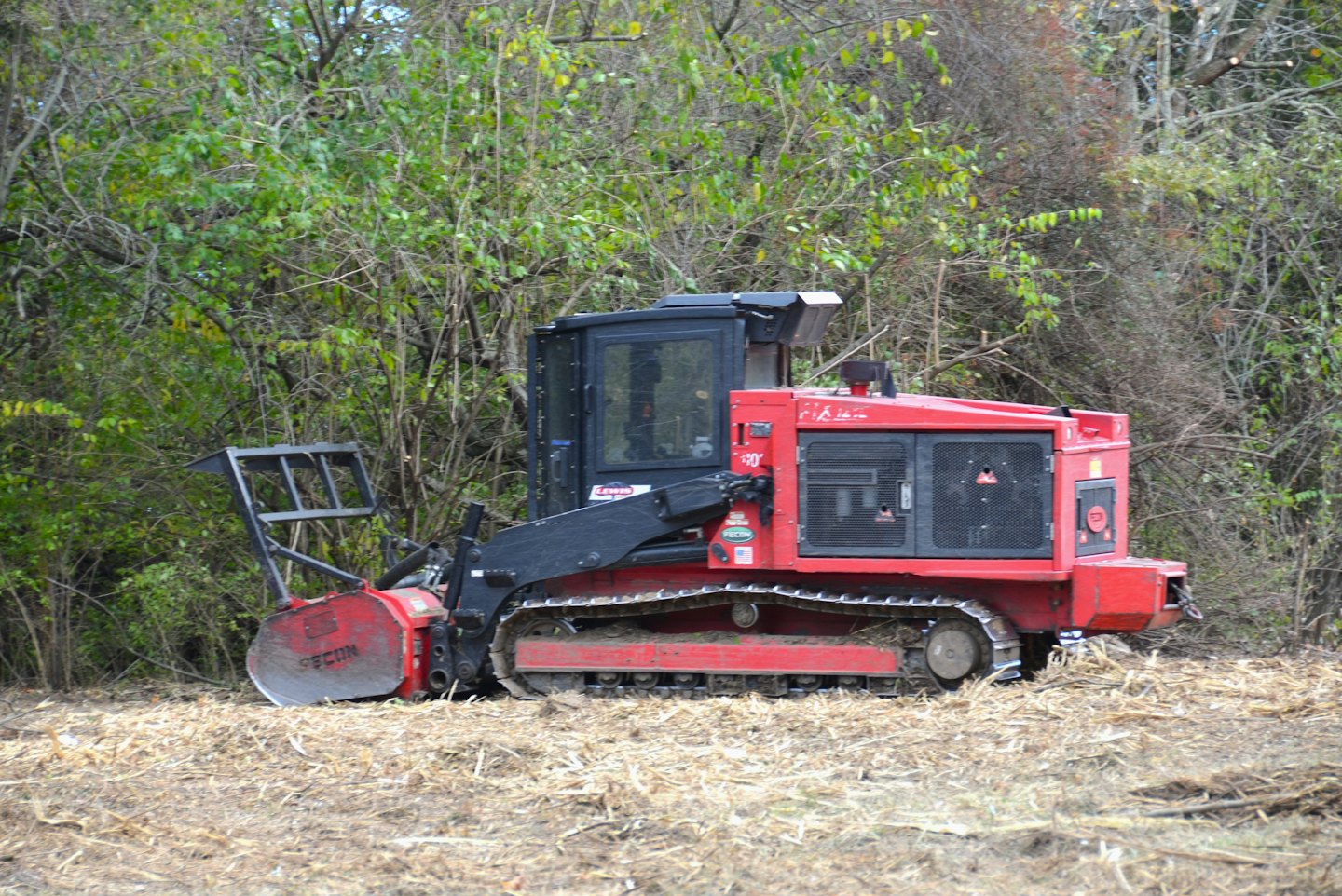 A red and black tracked mulcher clears wood in the forest.