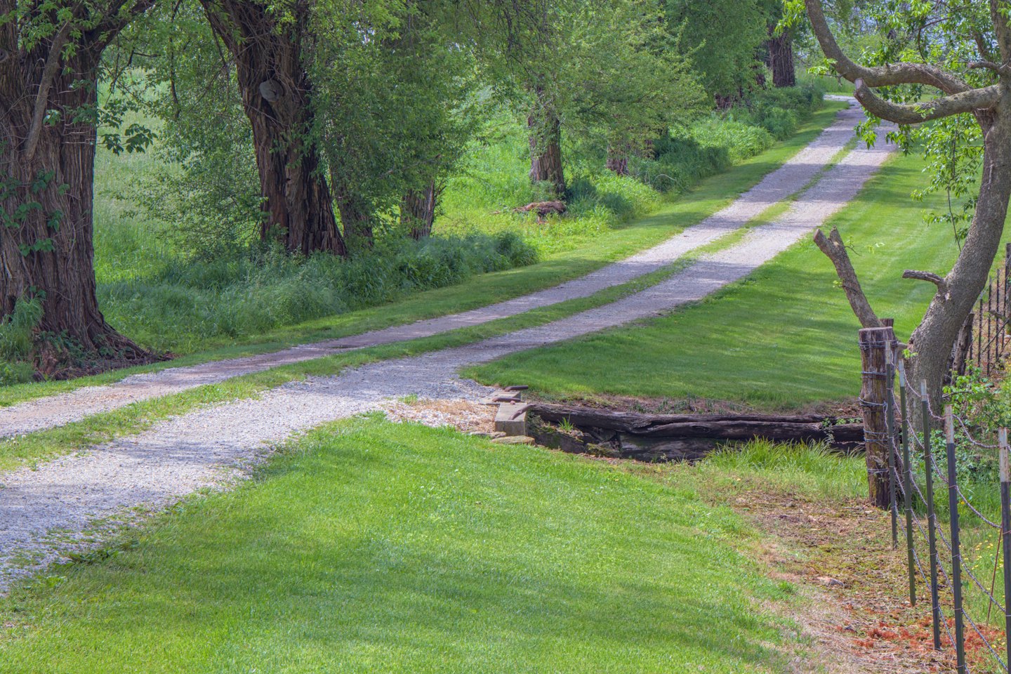 Gravel driveway winds through a green rural landscape with trees.