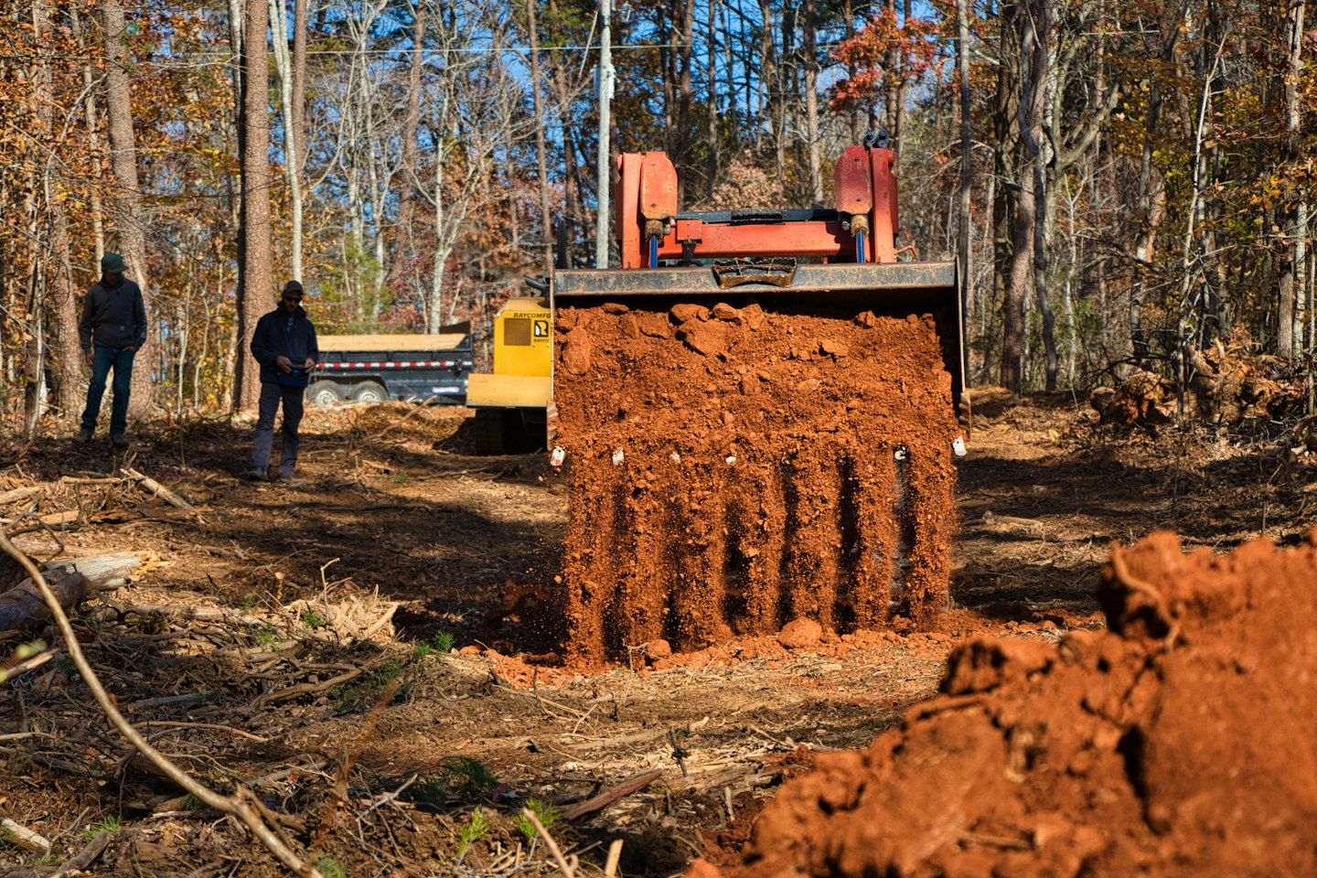 An excavator empties soil in a forest clearing.